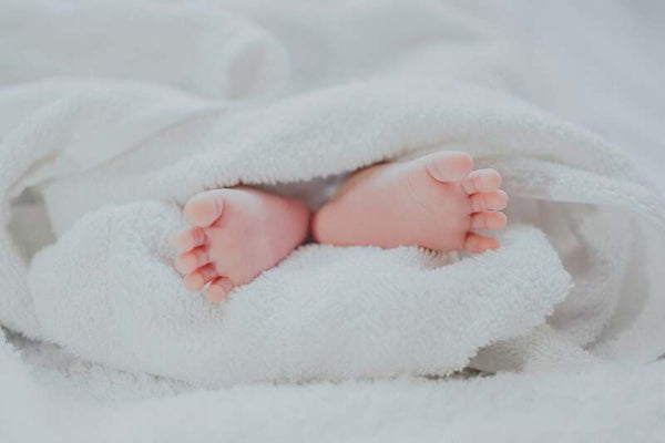 Close-up of a newborn baby's tiny feet peeking out from a soft white blanket