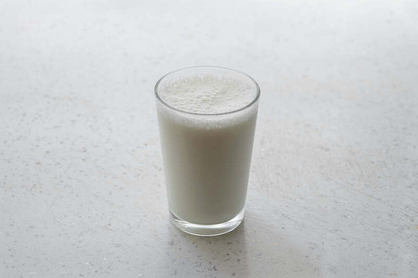 Glass of milk with a frothy top on a light surface