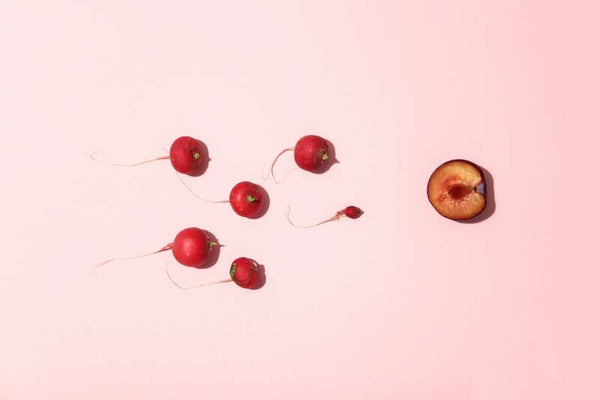 Radishes and a halved plum arranged on a pink background