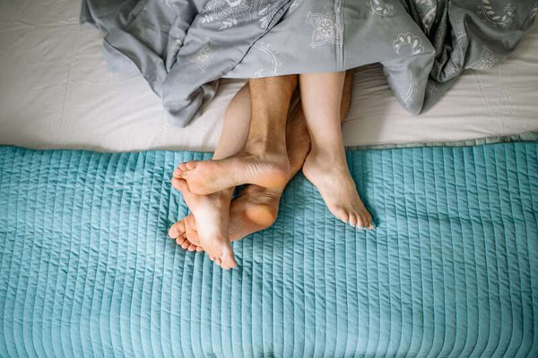 Overhead shot of a couple's bare feet peeking out from under a blanket on a bed