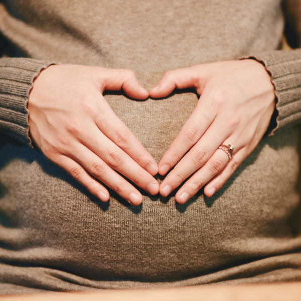 Close-up of hands forming a heart shape over a pregnant belly