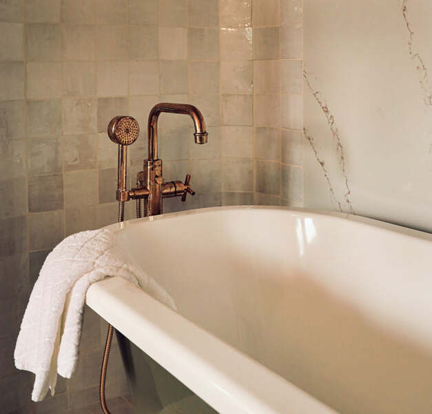 Close-up of a freestanding bathtub with a copper tap and folded white towel against patterned tiles