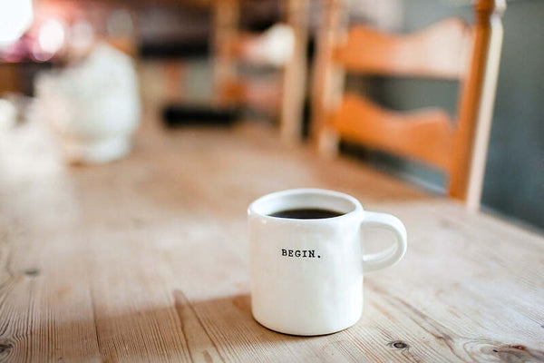 White mug printed with the word 'BEGIN' on a wooden table