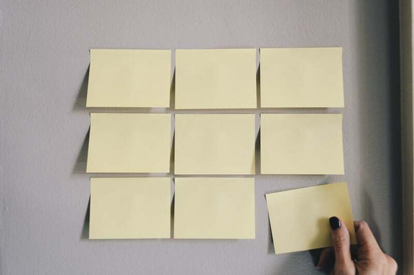Hand placing yellow sticky notes in a grid pattern on a wall