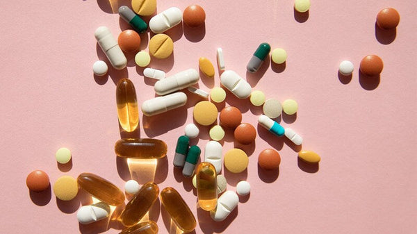 Assorted vitamin and supplement pills and capsules scattered on a pink background