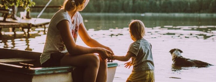 Mother and young child sitting together at the edge of a boat by a calm lake at sunset