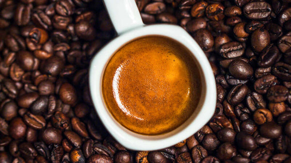 Overhead view of an espresso cup surrounded by roasted coffee beans