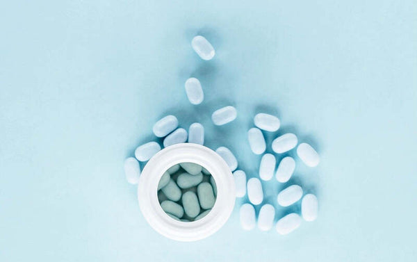 White pills spilling out of an open bottle on a blue background