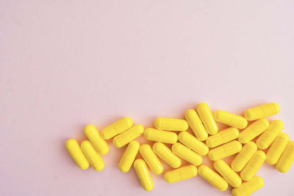 Yellow supplement capsules scattered on a pink background