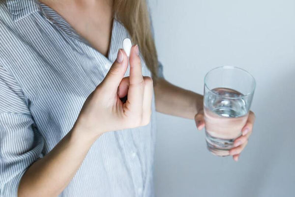 Woman holding a white supplement pill and a glass of water