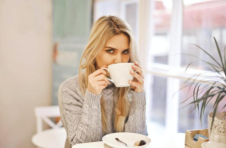 Woman drinking from a white mug at a cafe table