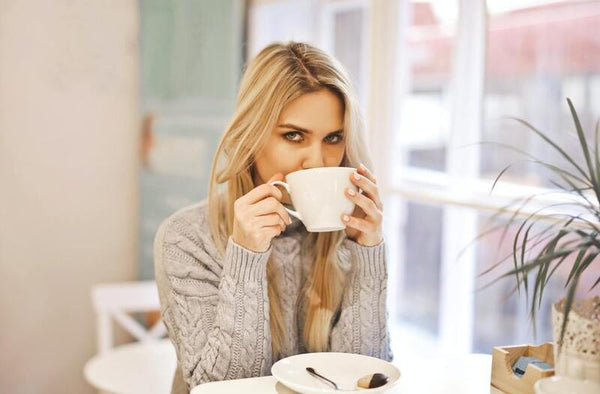 Woman drinking from a white mug at a cafe table