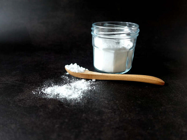Jar of white powder with a wooden spoon scattering powder on a dark surface