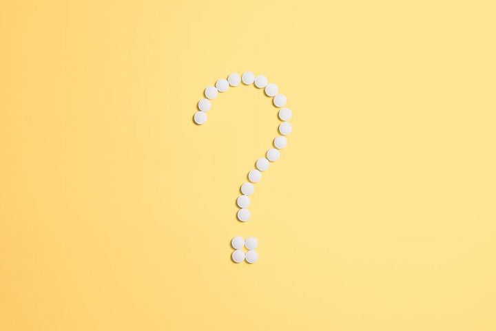 White pills arranged to form a question mark shape on a yellow background