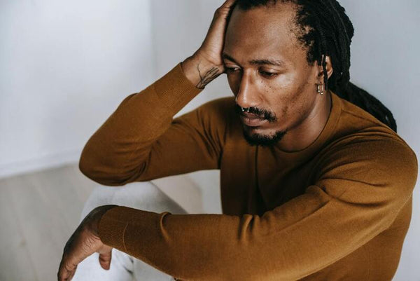 Man sitting with his hand on his head, looking down pensively