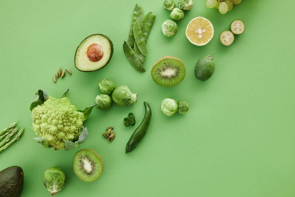 Overhead flat-lay of green vegetables and fruits including avocado, kiwi and brussels sprouts