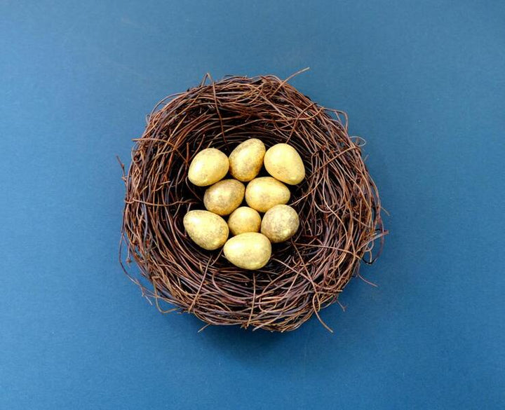 Golden decorative eggs nestled in a twig nest on a blue background