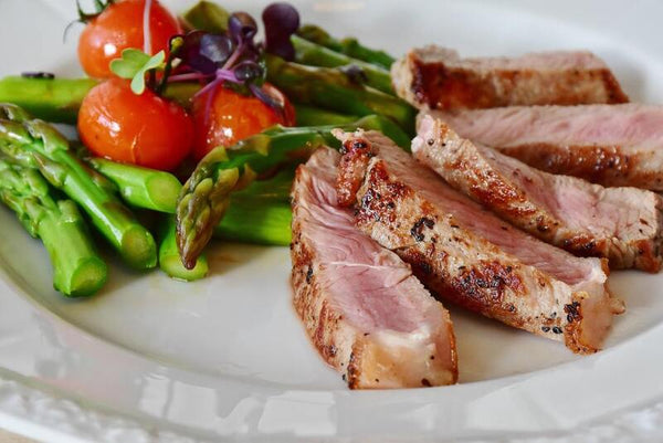 Sliced grilled steak served with cherry tomatoes and asparagus on a white plate