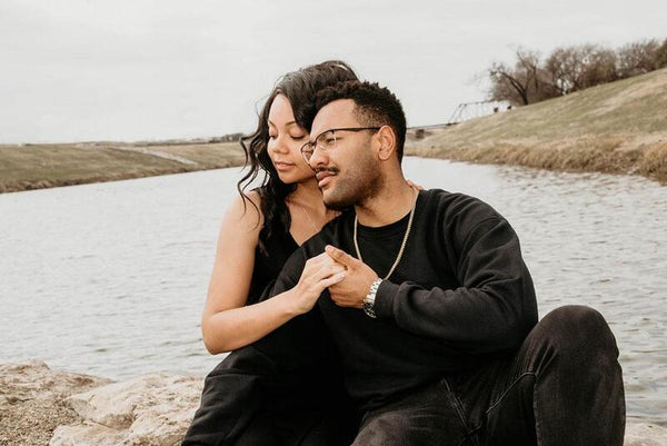 Couple sitting closely together holding hands beside a river