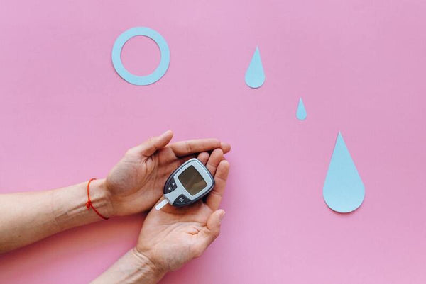 Hands holding a blood glucose monitor beside paper cutouts of a ring and droplets
