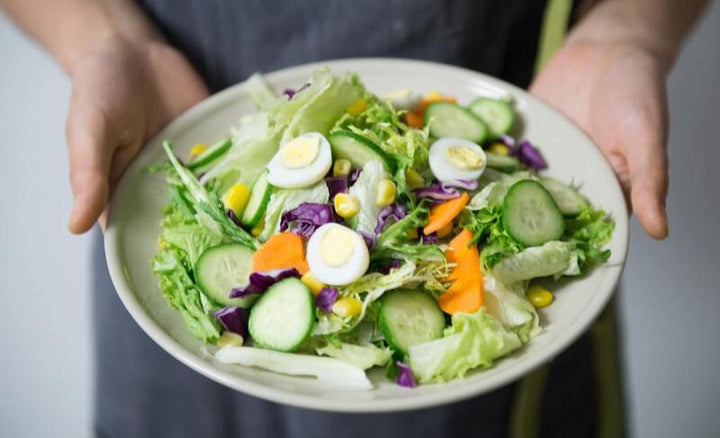 Woman holding a bowl of fresh garden salad with hard-boiled eggs and vegetables