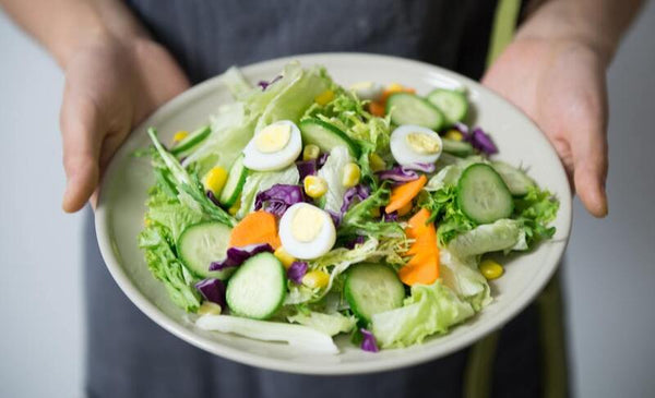 Woman holding a bowl of fresh garden salad with hard-boiled eggs and vegetables