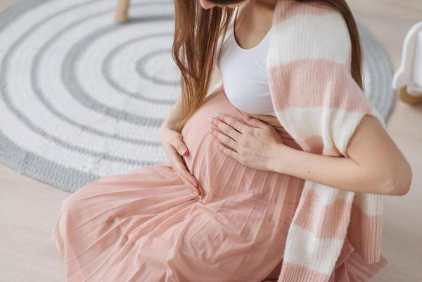 Pregnant woman in a pink dress sitting on the floor cradling her belly with both hands