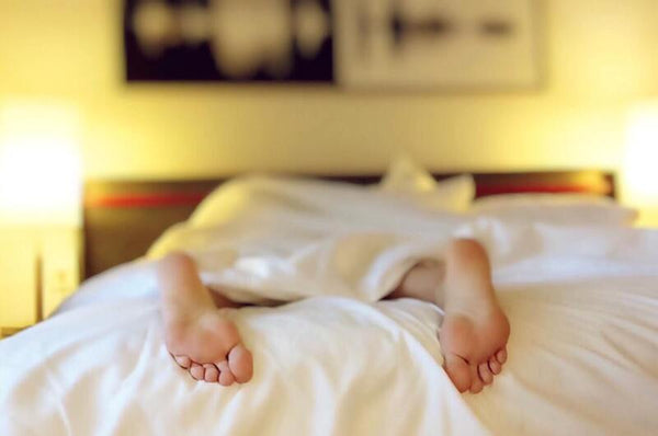 Bare feet poking out from under a white duvet at the end of a bed