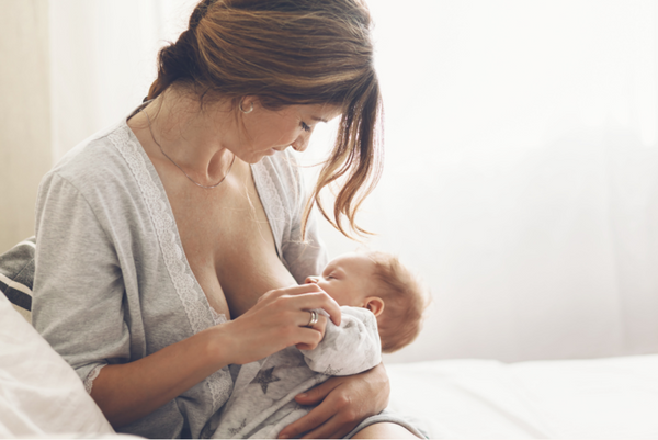 Woman in a robe breastfeeding her baby by a bright window