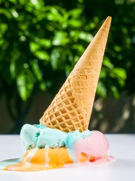 Melting ice cream cone with scoops dripping onto a white surface outdoors