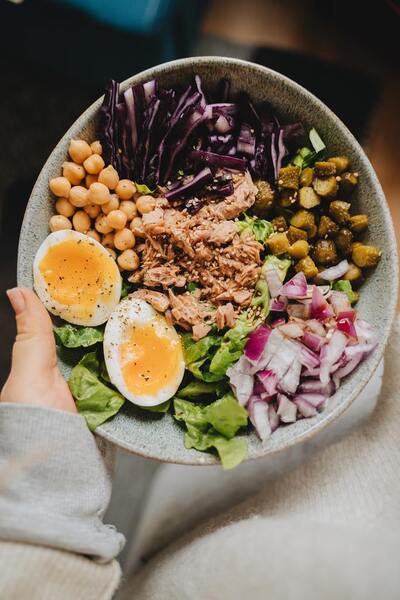 Hand holding a bowl of tuna salad with soft-boiled eggs, chickpeas and red cabbage