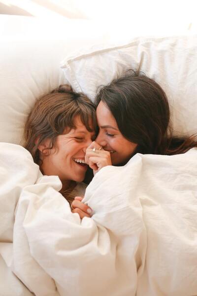Two women laughing together wrapped in white bedsheets