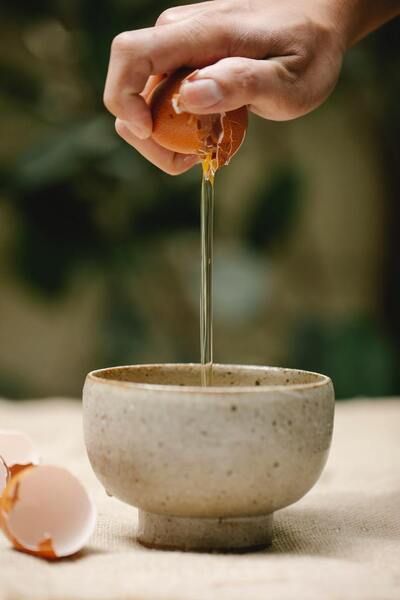 Hand cracking an egg into a small ceramic bowl