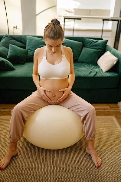 Pregnant woman sitting on an exercise ball with her hands on her belly in a living room