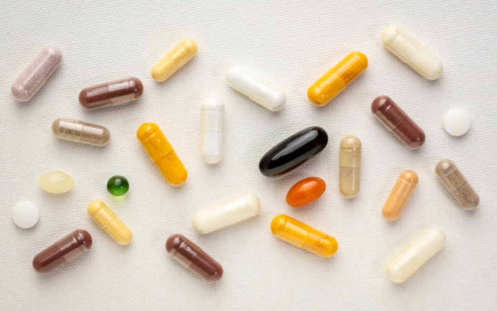 Assorted vitamins and supplement capsules in various colours and sizes scattered on a white surface