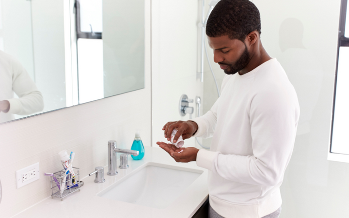 Man in a white jumper pouring supplement capsules into his hand at a bathroom sink