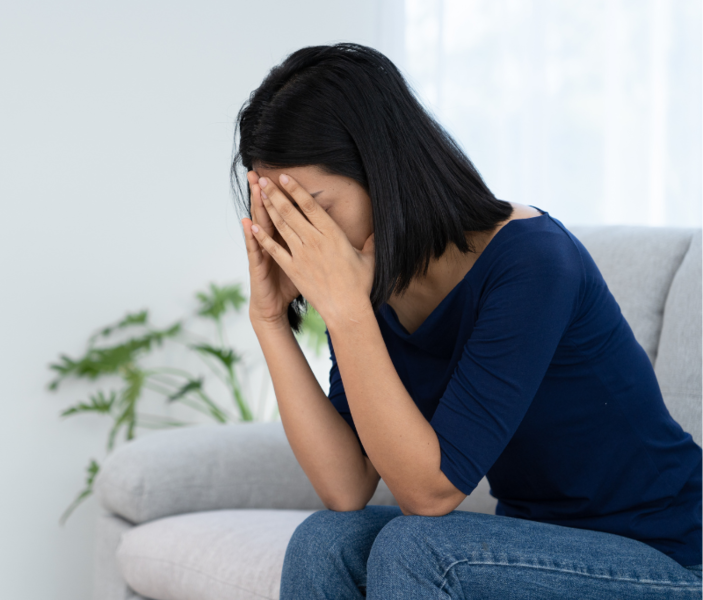 Woman sitting on a sofa with her head in her hands, looking distressed