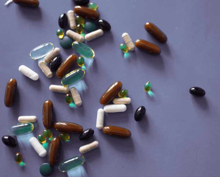 Assorted supplement capsules and softgels in brown, black, white and green scattered on a grey surface