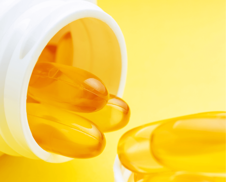 Golden omega-3 gel capsules spilling from a white bottle on a yellow background
