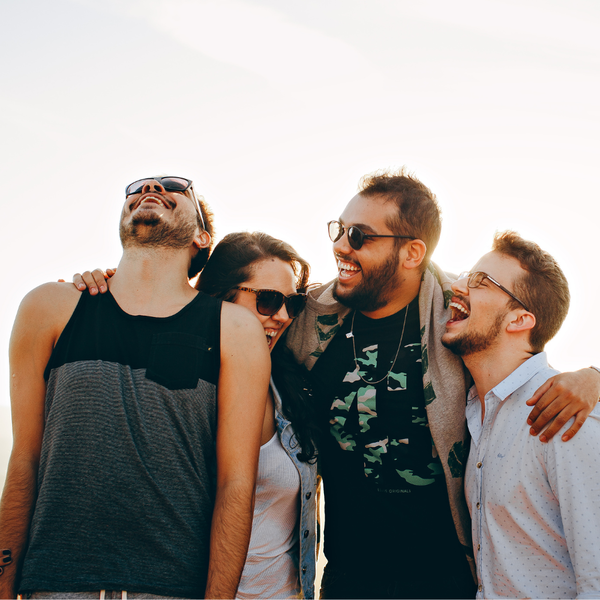 Four friends laughing together outdoors wearing sunglasses