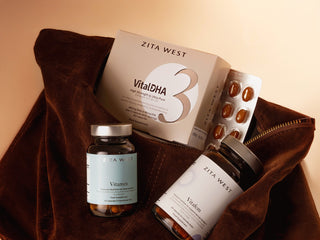 Zita West products arranged in an open brown velvet pouch against a warm beige background, including a Vital DHA box, a Vitamen bottle, a Vitafem bottle, and a blister pack of capsules.