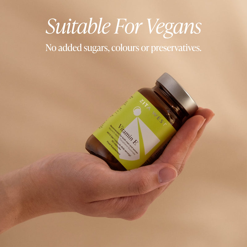 Hand holding a vitamin E bottle with a green label, set against a beige background.